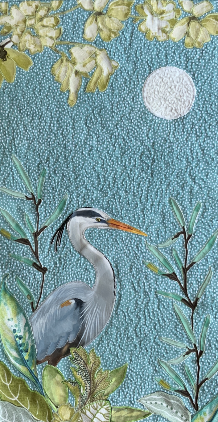 Blue heron stands in the marsh amidst a background of reeds and blue sky.