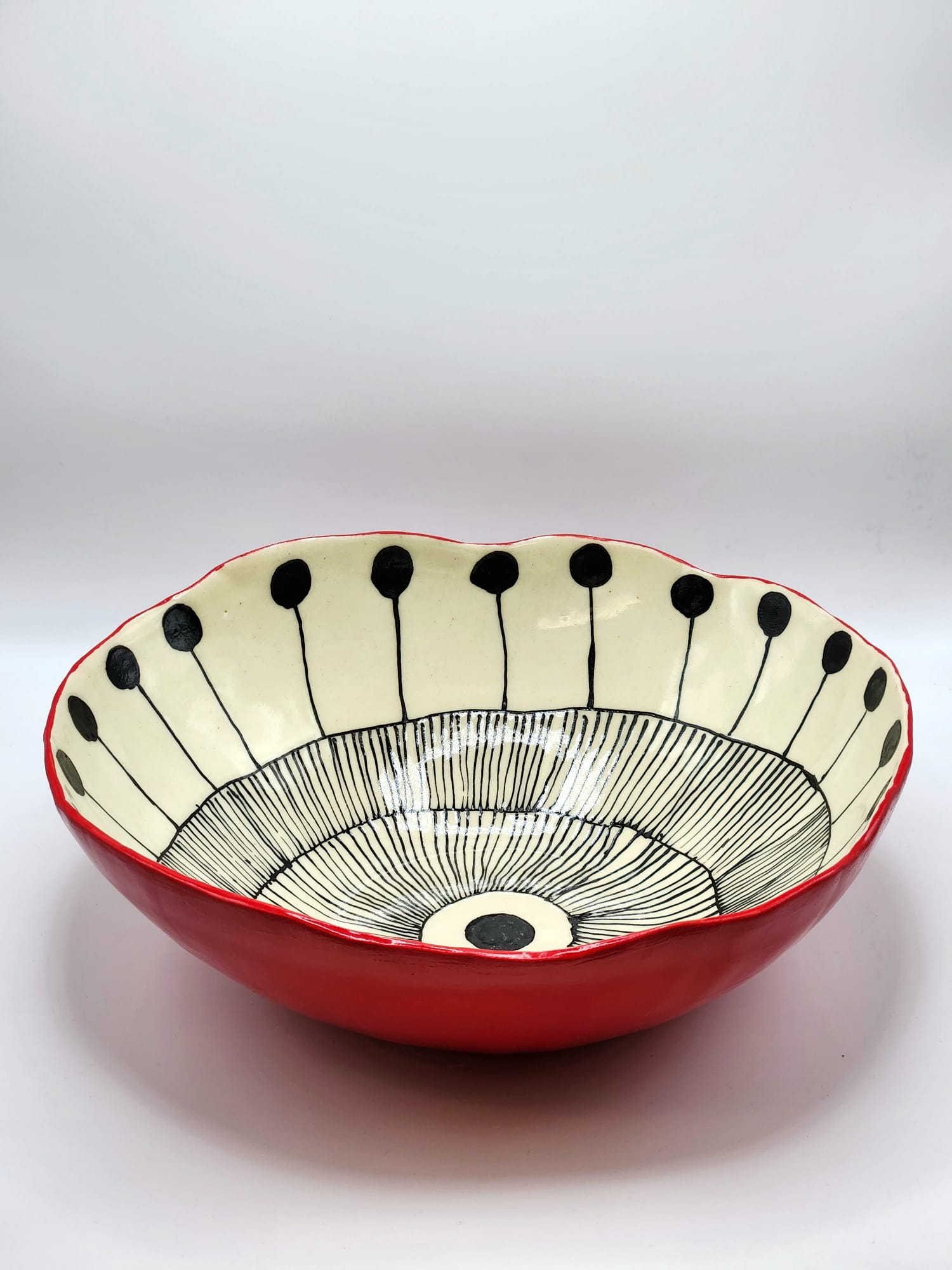 A hand-built porcelain bowl showcases a striking contrast between its black underglaze pattern of circles and lines and its vibrant red underglaze exterior. A final coat of clear glaze on both surfaces brings out the depth of color and the delicate nature of the porcelain.