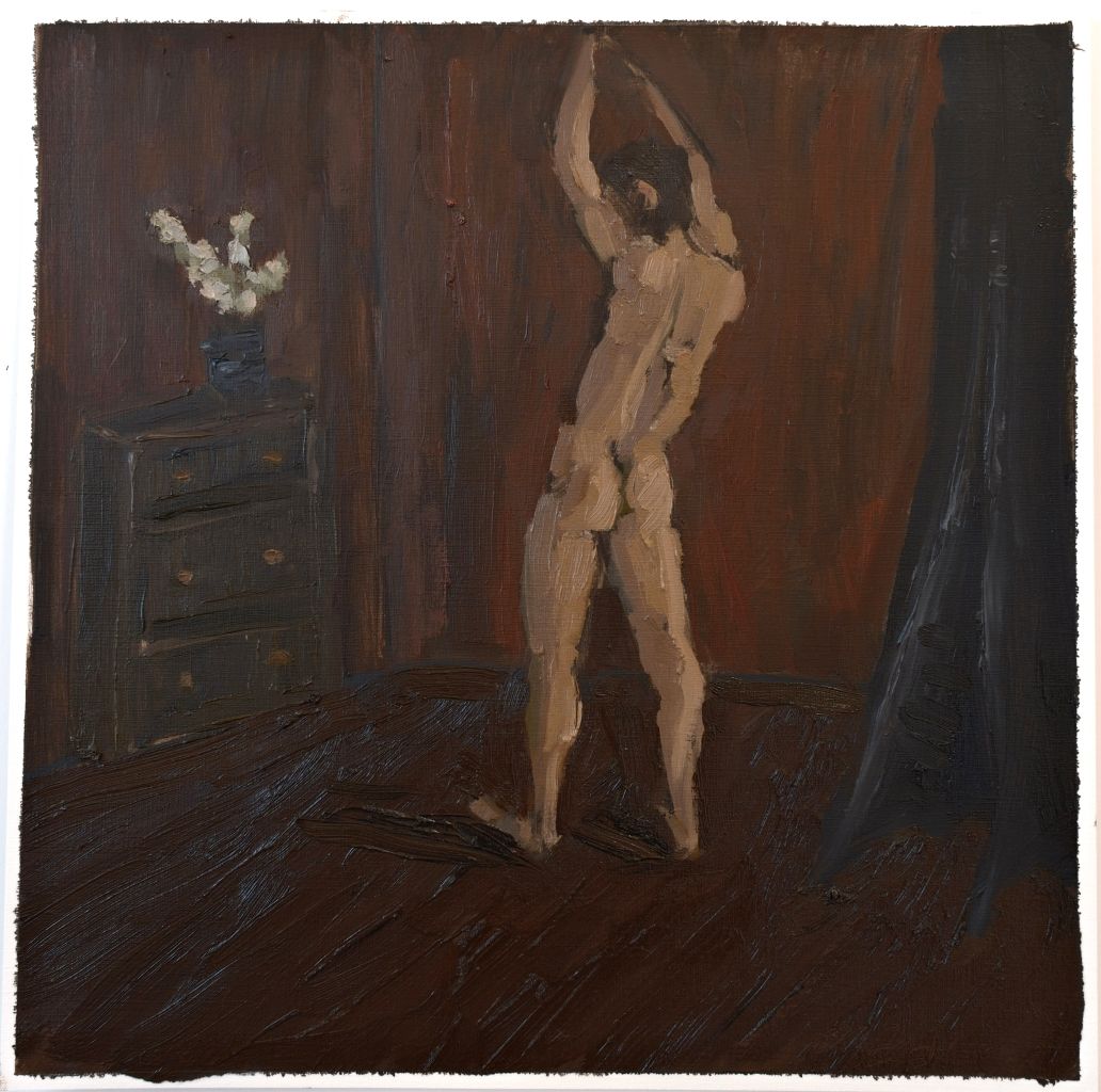 Naked boy with raised arms in dark room beside white flowers on dresser. 